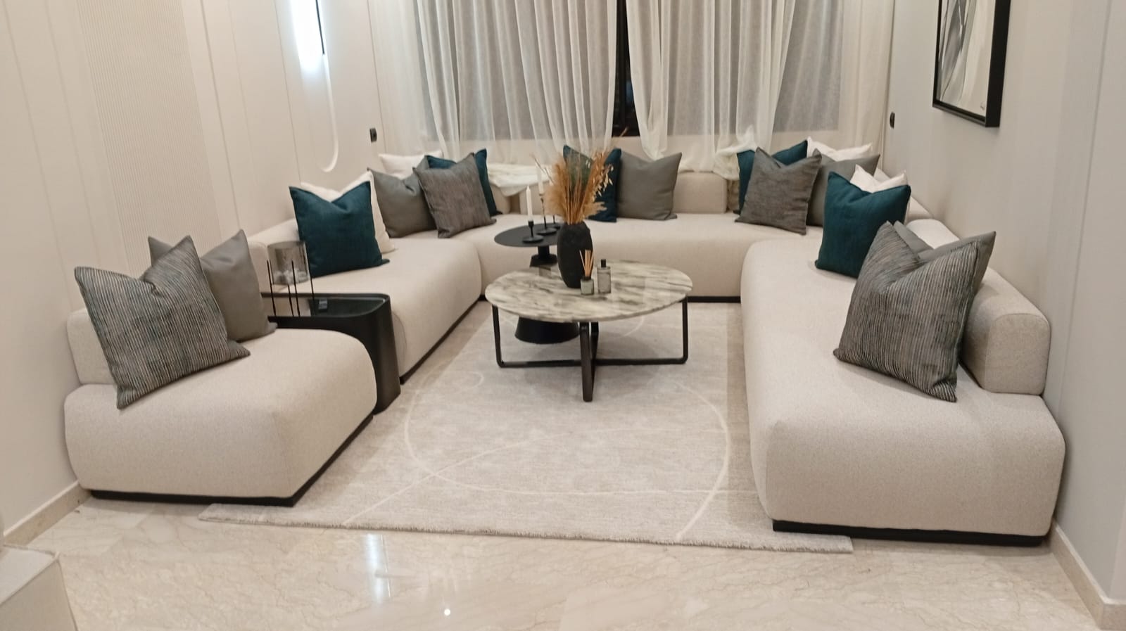 Salon avec un canapé d'angle en tissu clair et des coussins gris et bleu canard