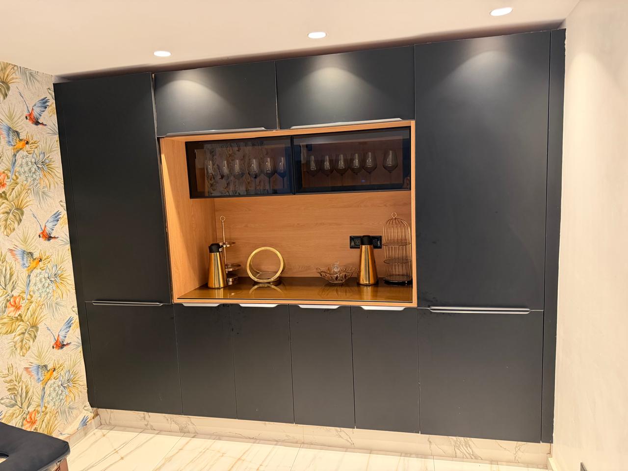 Mur de rangements gris foncé avec une niche en bois clair éclairée, verres à pied sur les étagères