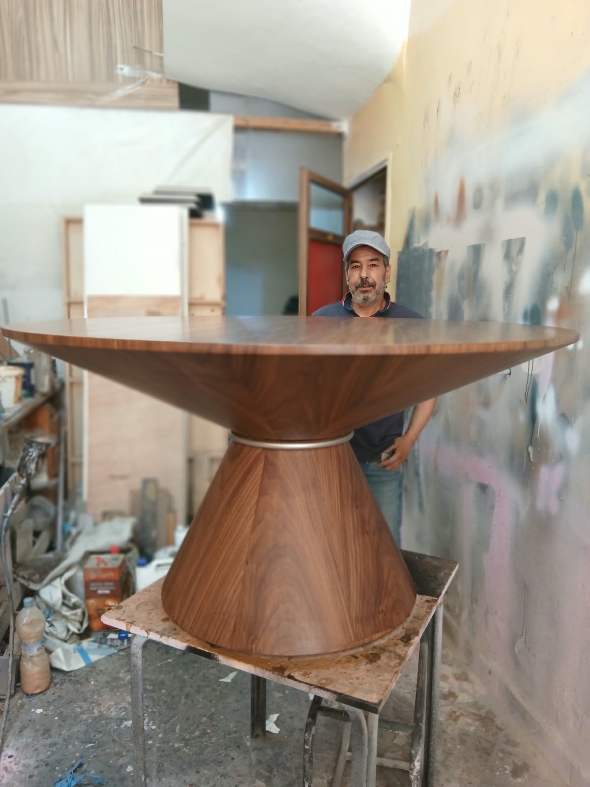 Table de salle à manger ronde en noyer sur un pied en double cône, à l'atelier, avec l'artisan derrière
