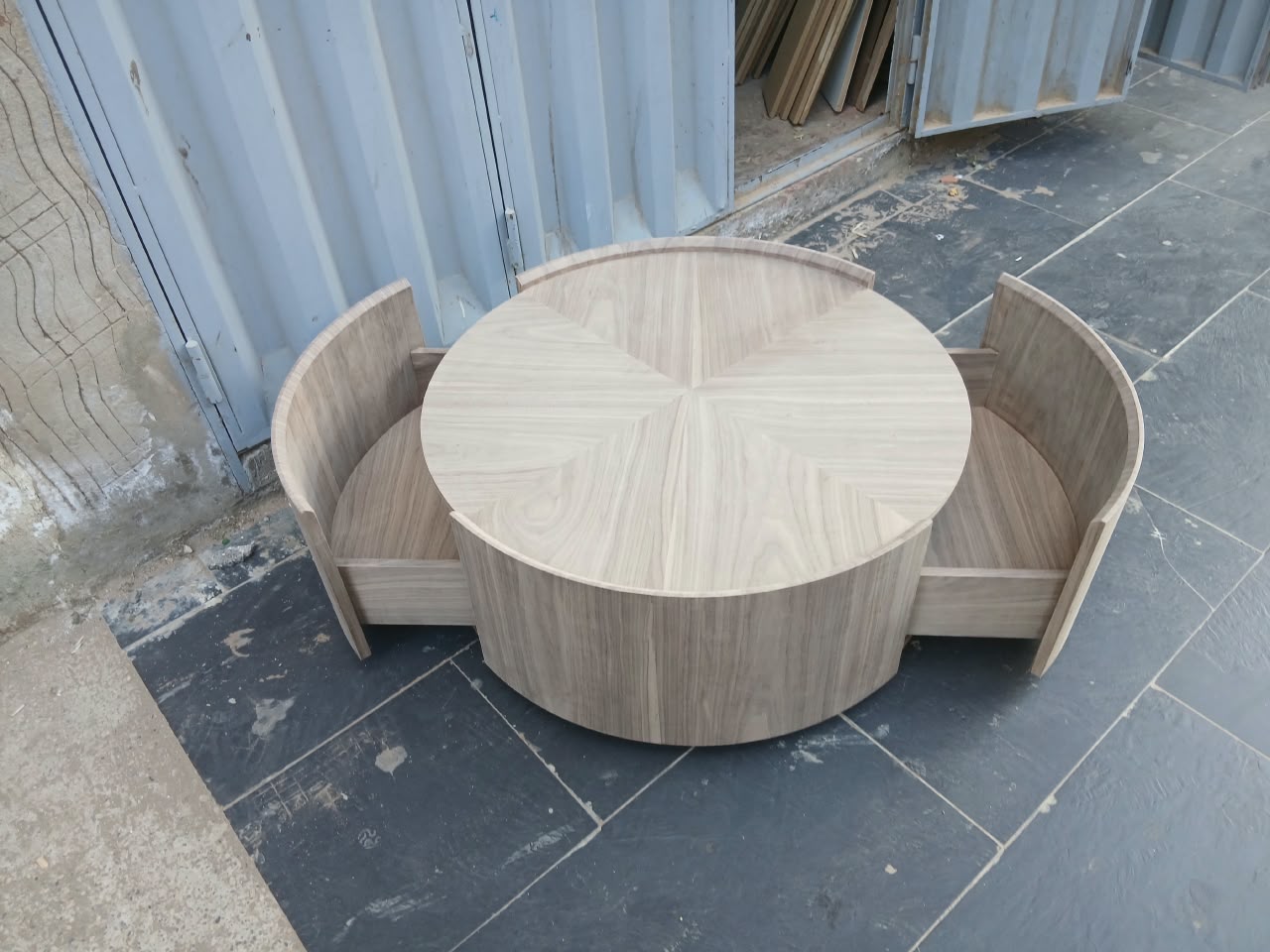 Table basse ronde en bois clair avec deux tiroirs courbes ouverts, devant l'atelier